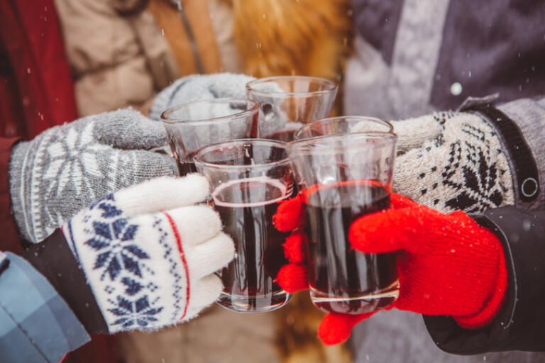 Close up of hands holding cups with hot wine. Friends cheering with glasses. Wearing warm knitted gloves.