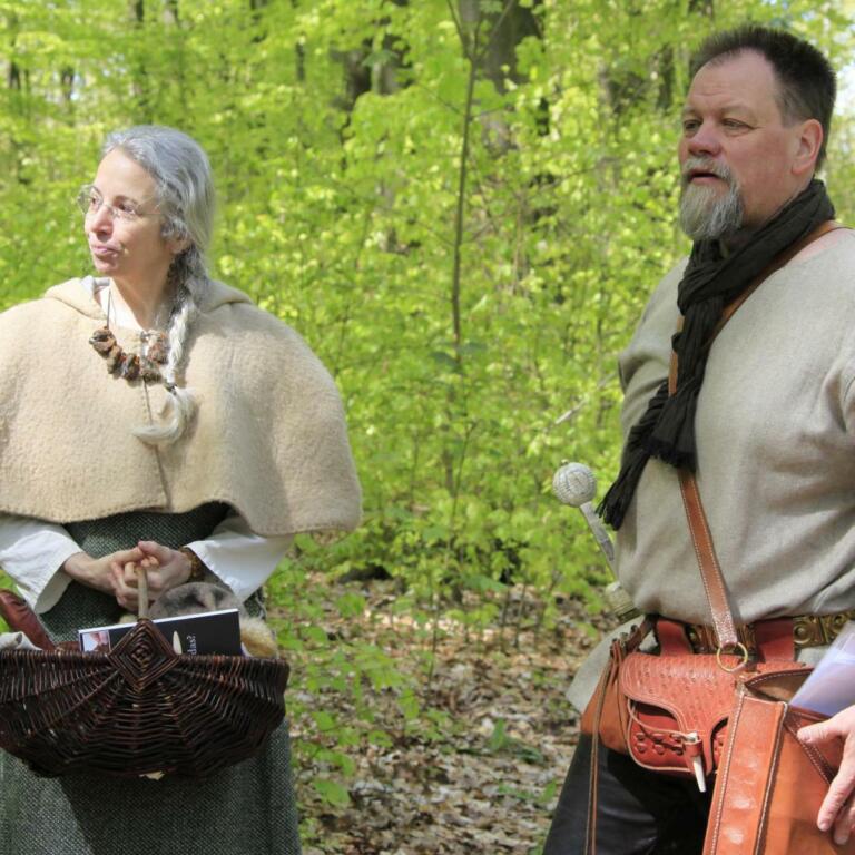 Zwei Personen in historischer Kleidung stehen in einem Waldgebiet, das an die Römerzeit erinnert, im Rahmen einer Römerwanderung entlang des Limes, organisiert von den Limes Cicerones.