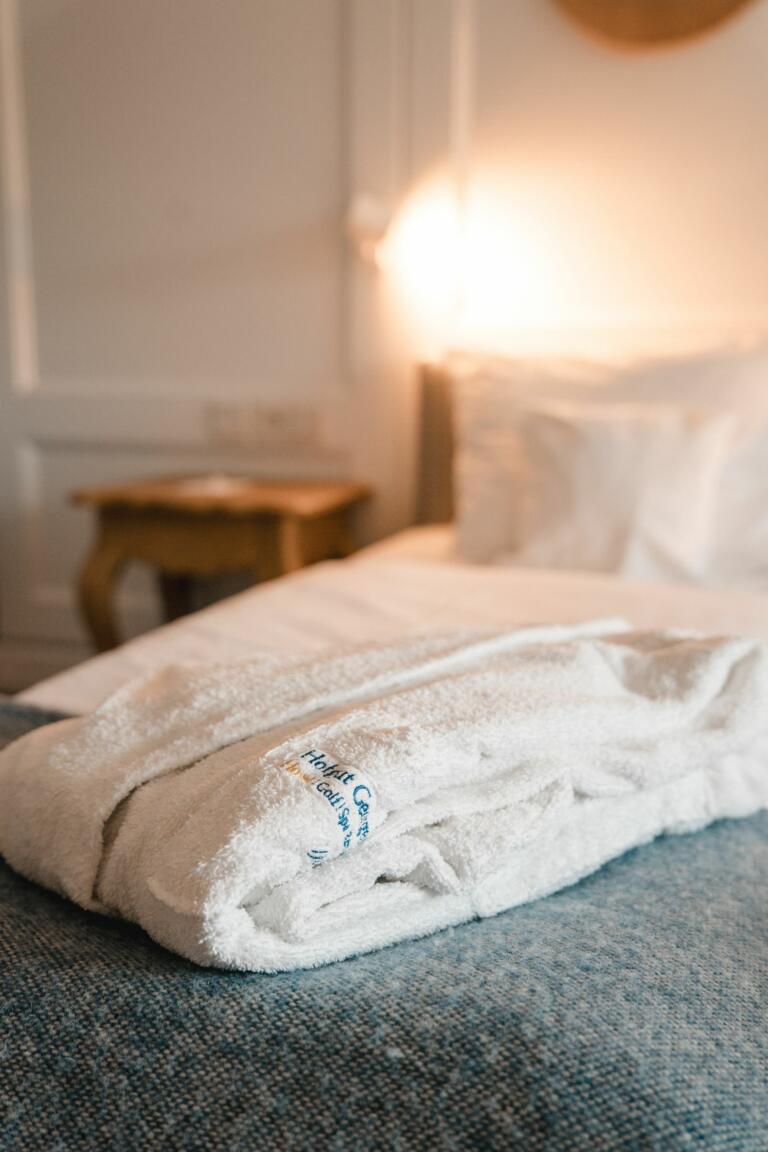Weißer Bademantel, der schön zusammengelegt ist und auf einem Bett liegt.