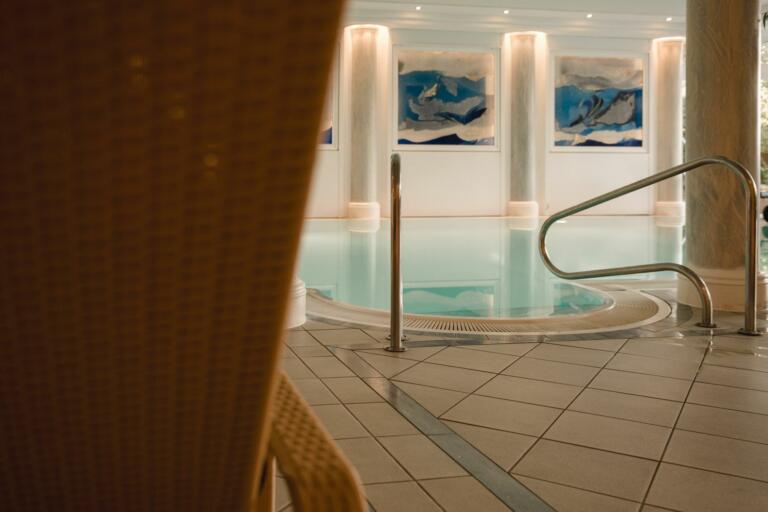 Der Wellnessbereich des Hofguts Georgenthal mit einem Innenpool, dessen türkisfarbenes Wasser sanft reflektiert.