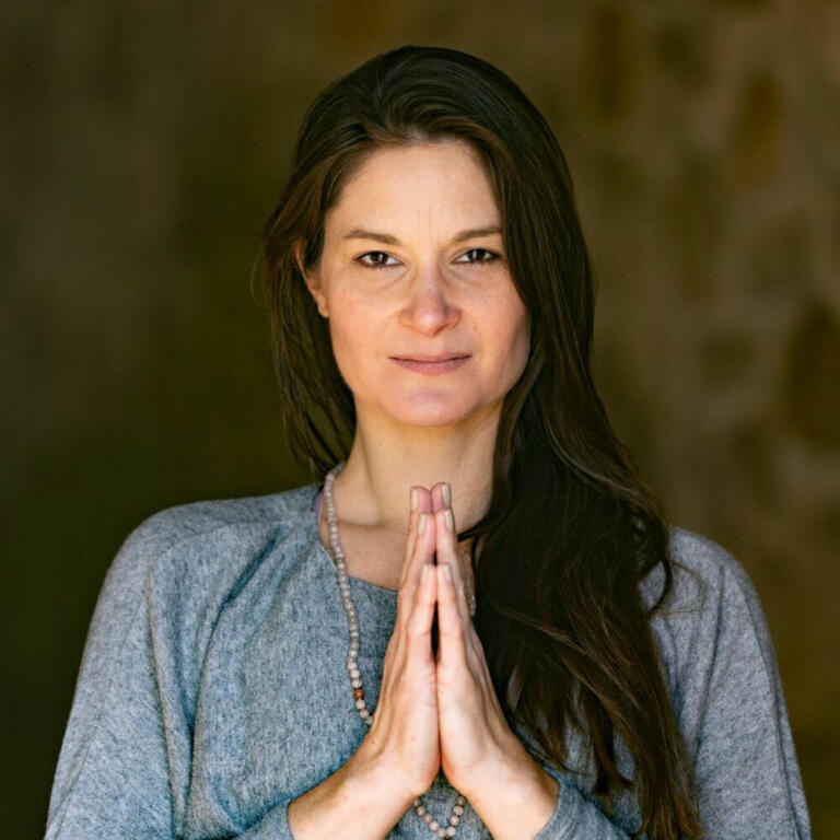 Eine Dame mit braunen langen Haaren, die den Namaste-Gruß macht.