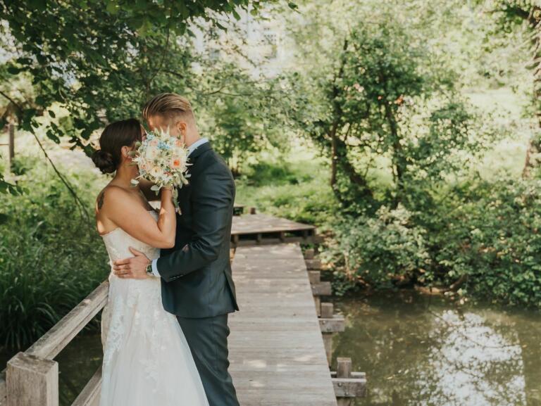 Romantischer Hochzeitsmoment im Hofgut Georgenthal: Ein Brautpaar steht auf einem Holzsteg am Wasser, umgeben von der grünen Natur des Taunus.