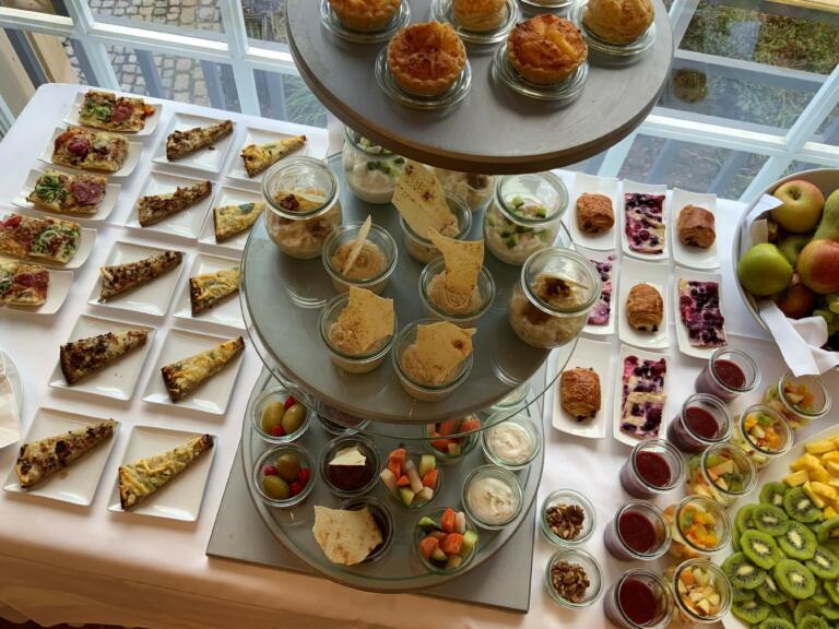 Buffet im Hofgut Georgenthal mit einem mehrstöckigen Etageren-Arrangement, gefüllt mit kleinen Speisen wie Quiches, Wraps, Desserts und Obst, umgeben von weiteren Platten mit Snacks und frischem Obst.