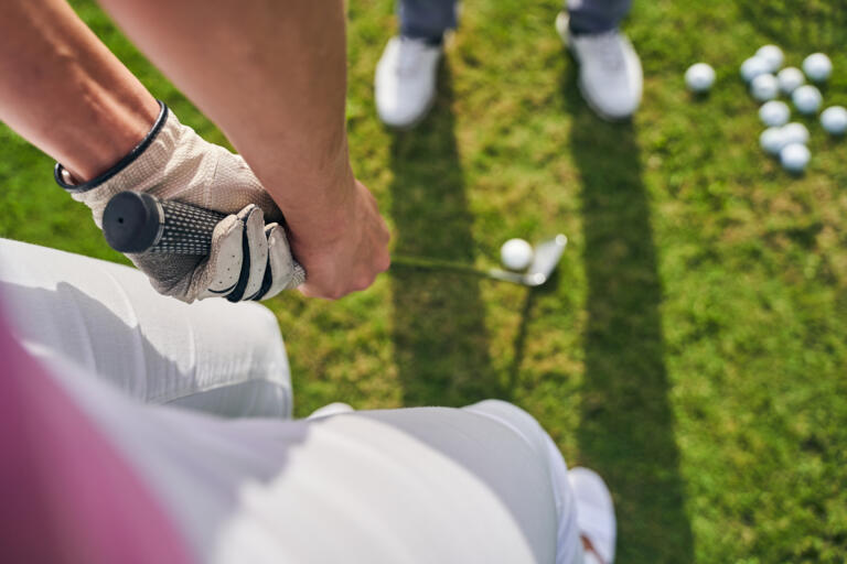 Nahaufnahme eines Golftrainings auf dem Golfplatz des Hofgut Georgenthal. Eine Person in Golfhandschuhen hält einen Schläger, während ein Coach oder Mitspieler daneben steht. Im Hintergrund liegen mehrere Golfbälle auf dem gepflegten Rasen.