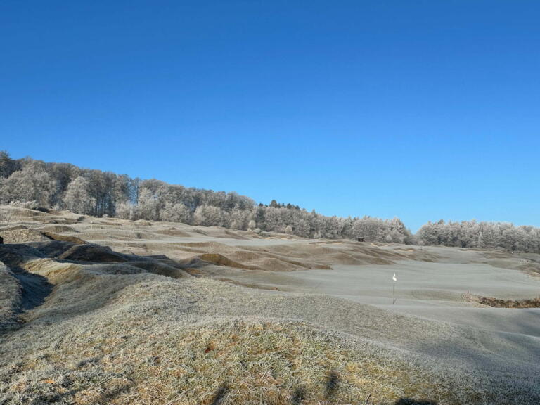 Winterliche Golfplatzlandschaft im Hofgut Georgenthal im Taunus mit frostbedeckten Fairways, sanften Hügeln und blauem Himmel.